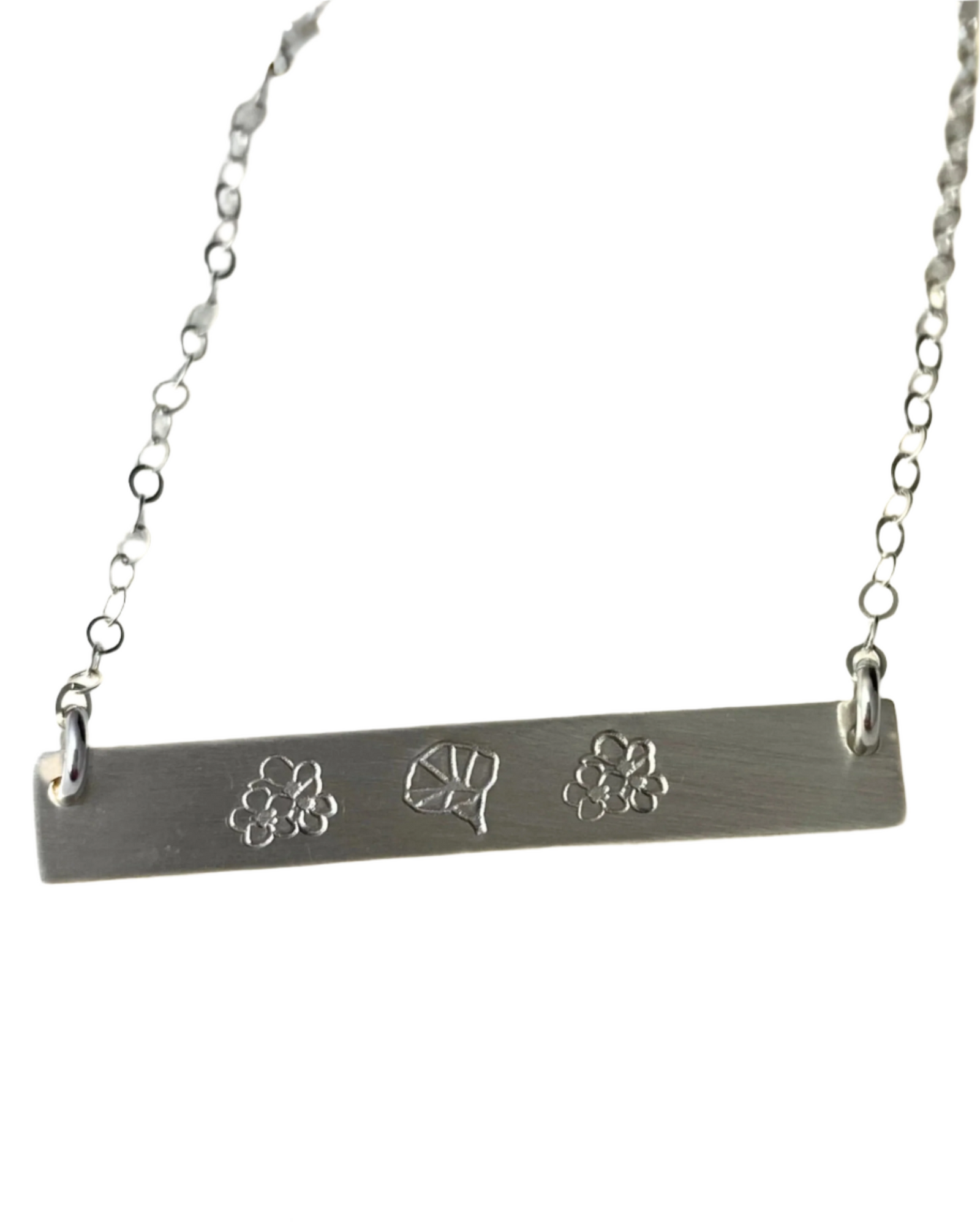 A sterling silver bar necklace with three engraved flowers on the front, attached to a chain.