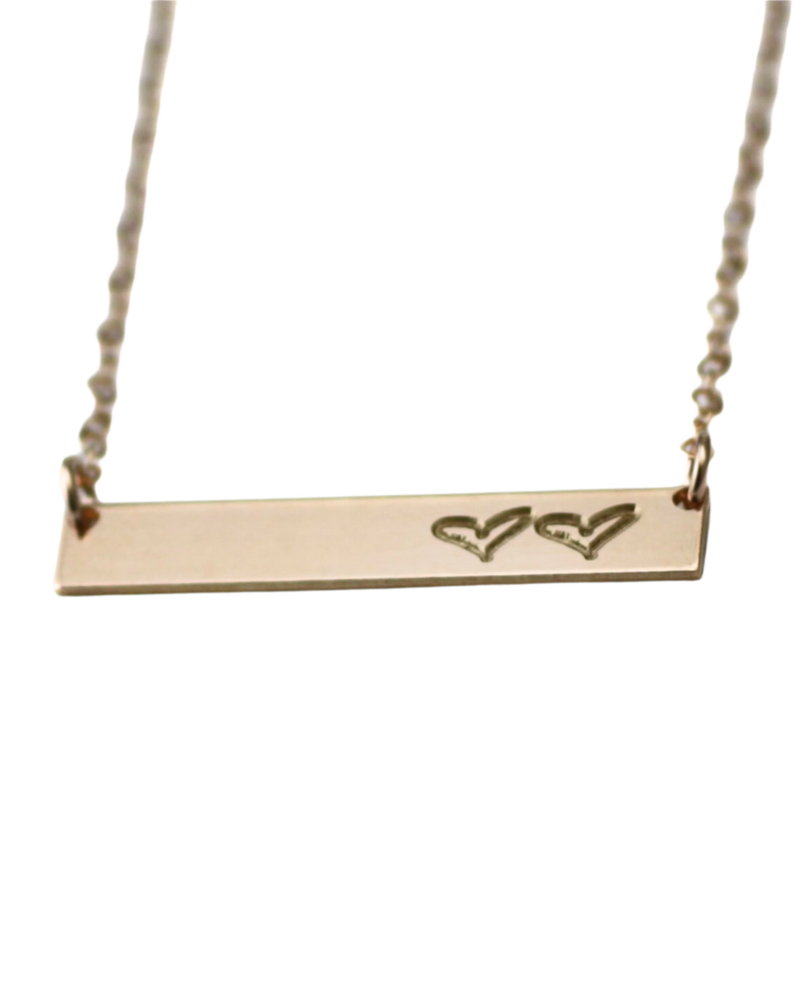 A gold-filled necklace with a bar pendant engraved with two hearts, on a white background.